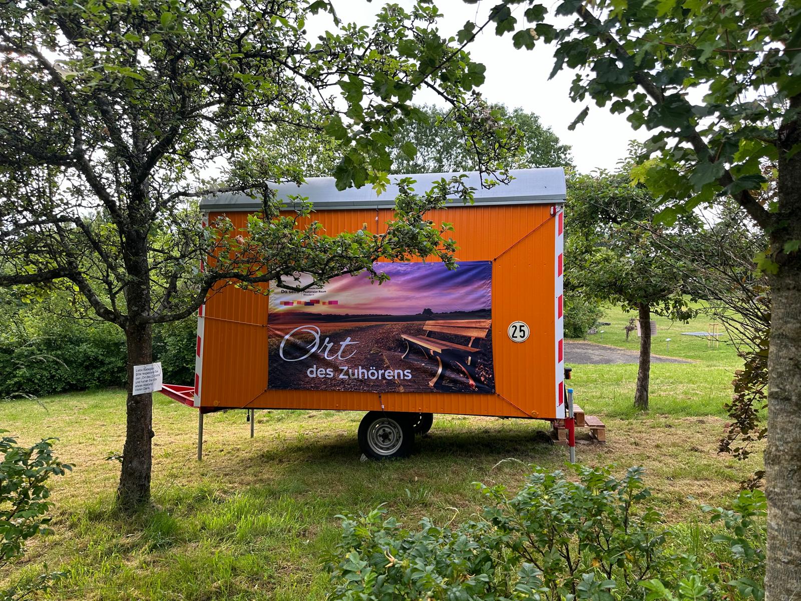 Bauwagen vor dem Losheimer Stausse mit dem Plakat 'Ort des Zuhörens'